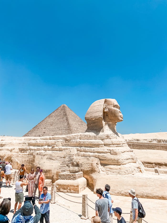 Tourists exploring the iconic Great Sphinx and Pyramid under a bright blue sky in Giza, Egypt.